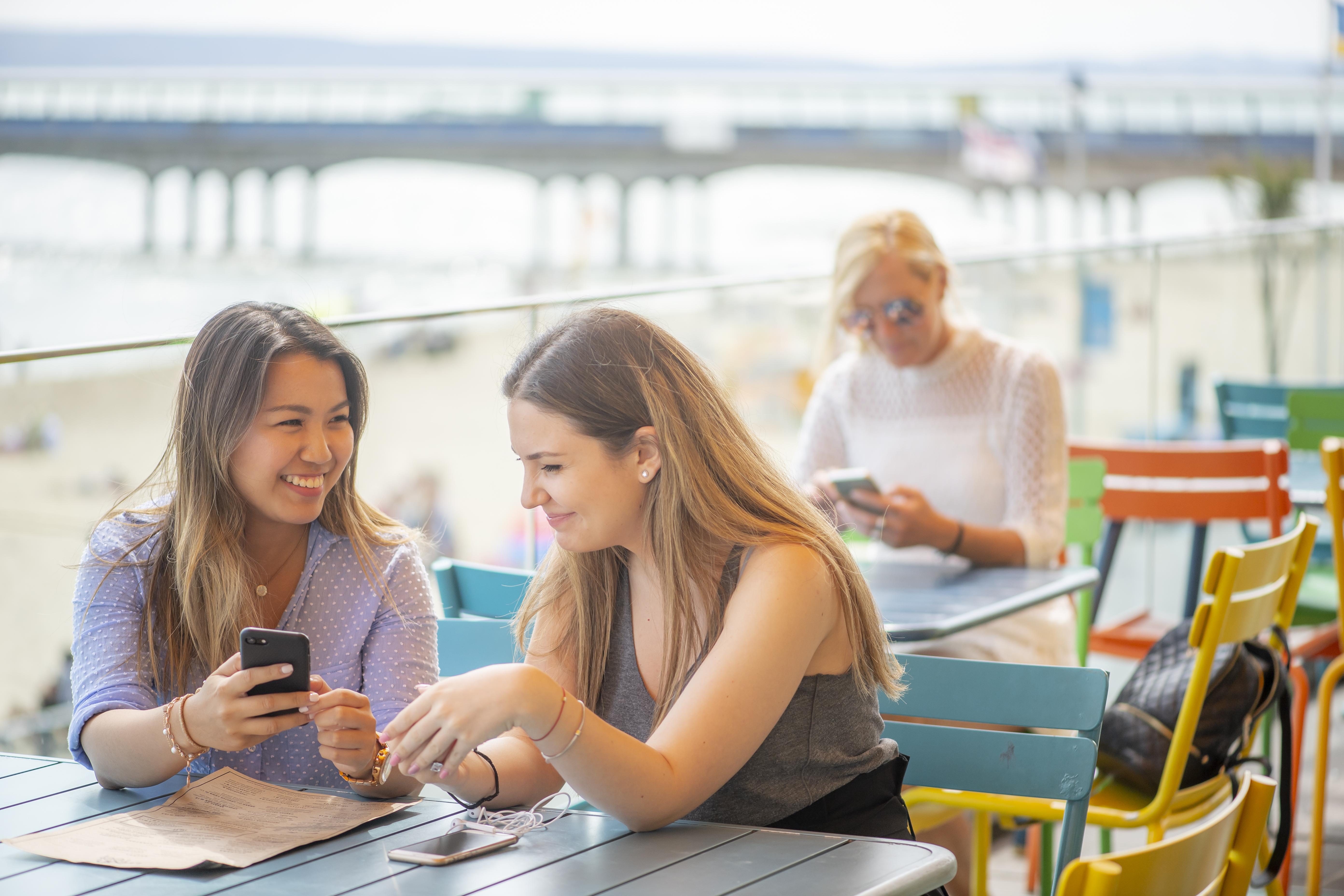 Two female students looking at their phones at a Boscombe beach side food place