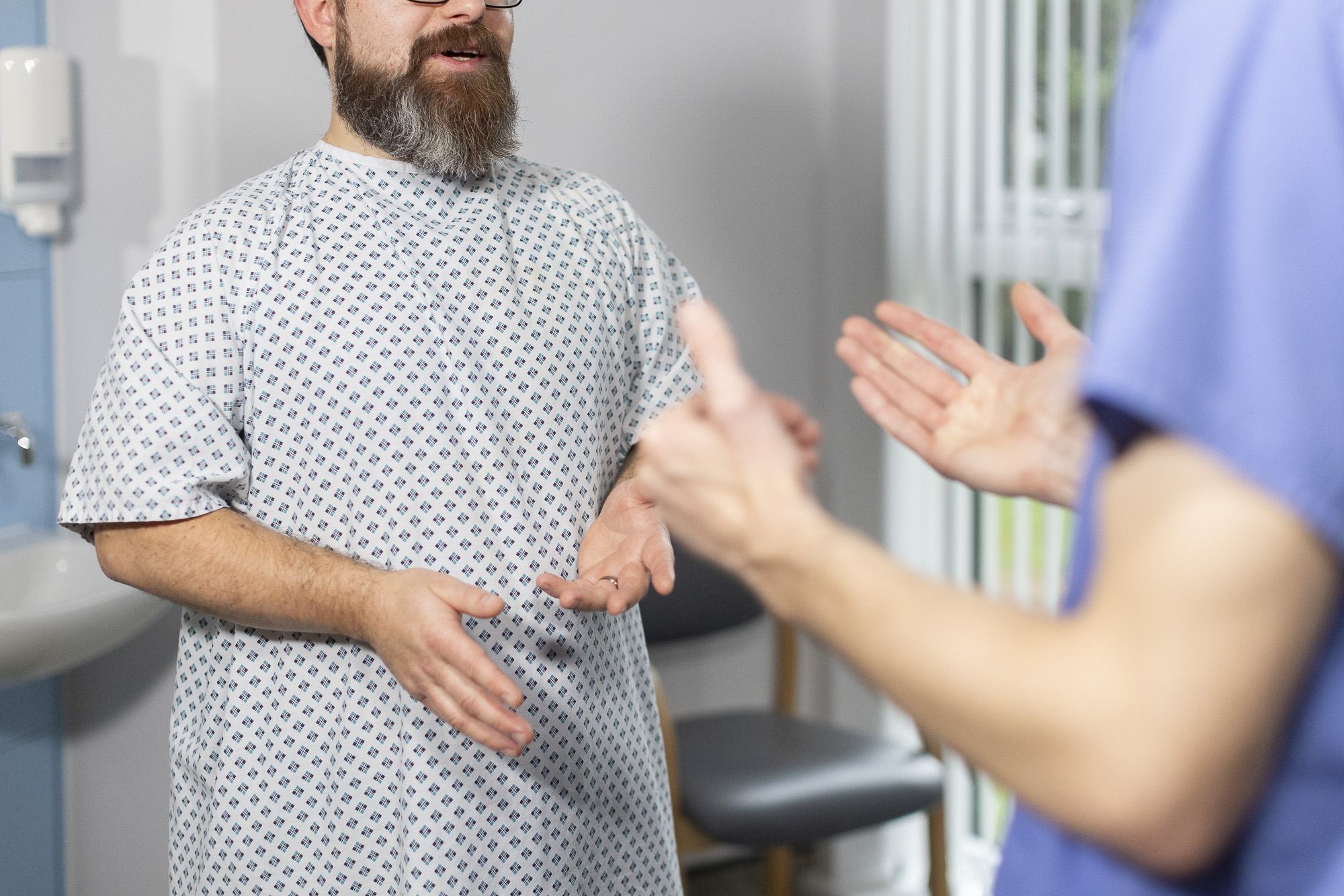 Person wearing scrubs speaking to a patient wearing hospital gown