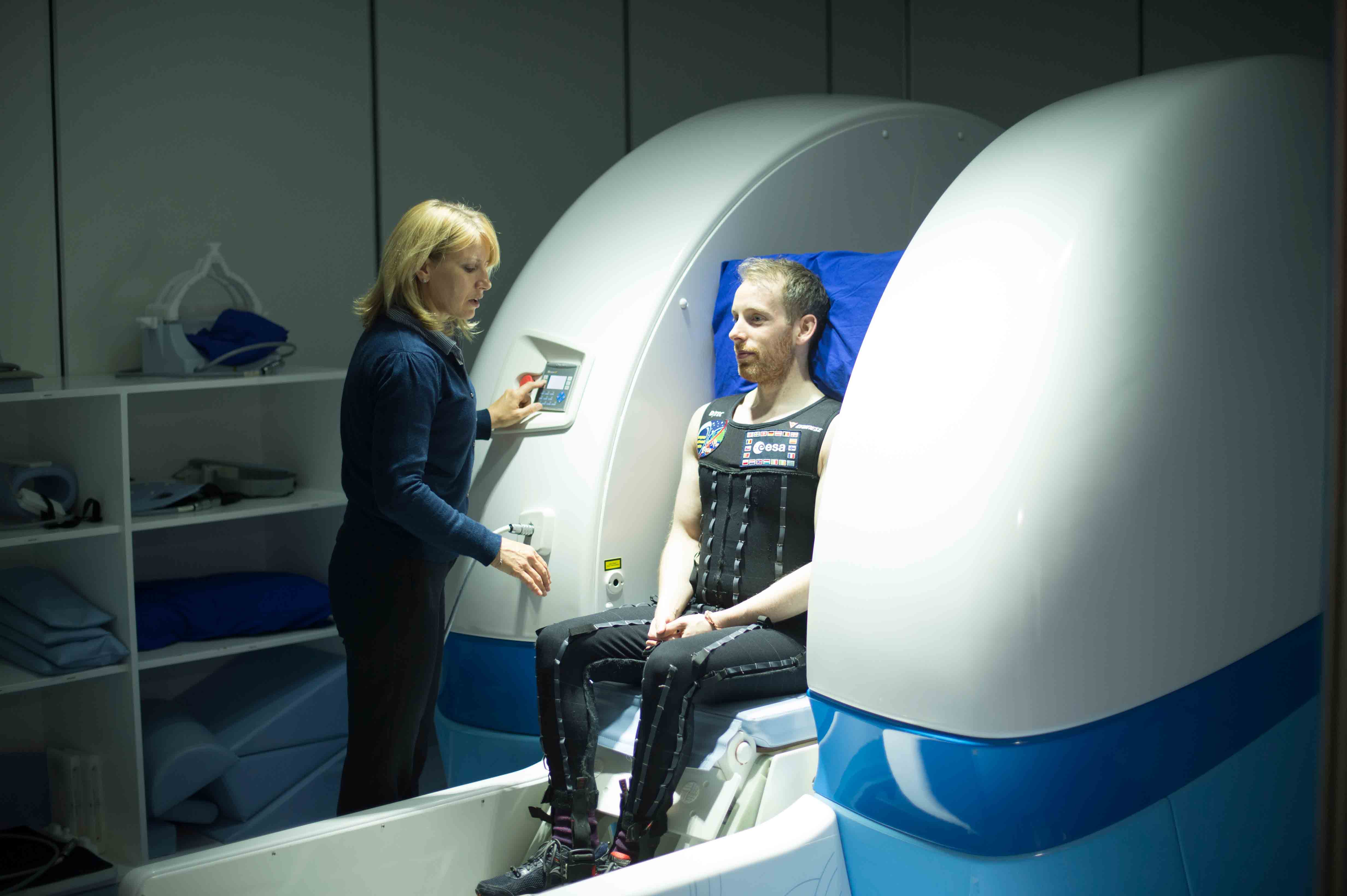 Patient sat in the open upright MRI scanner with a member of staff explaining the process to them